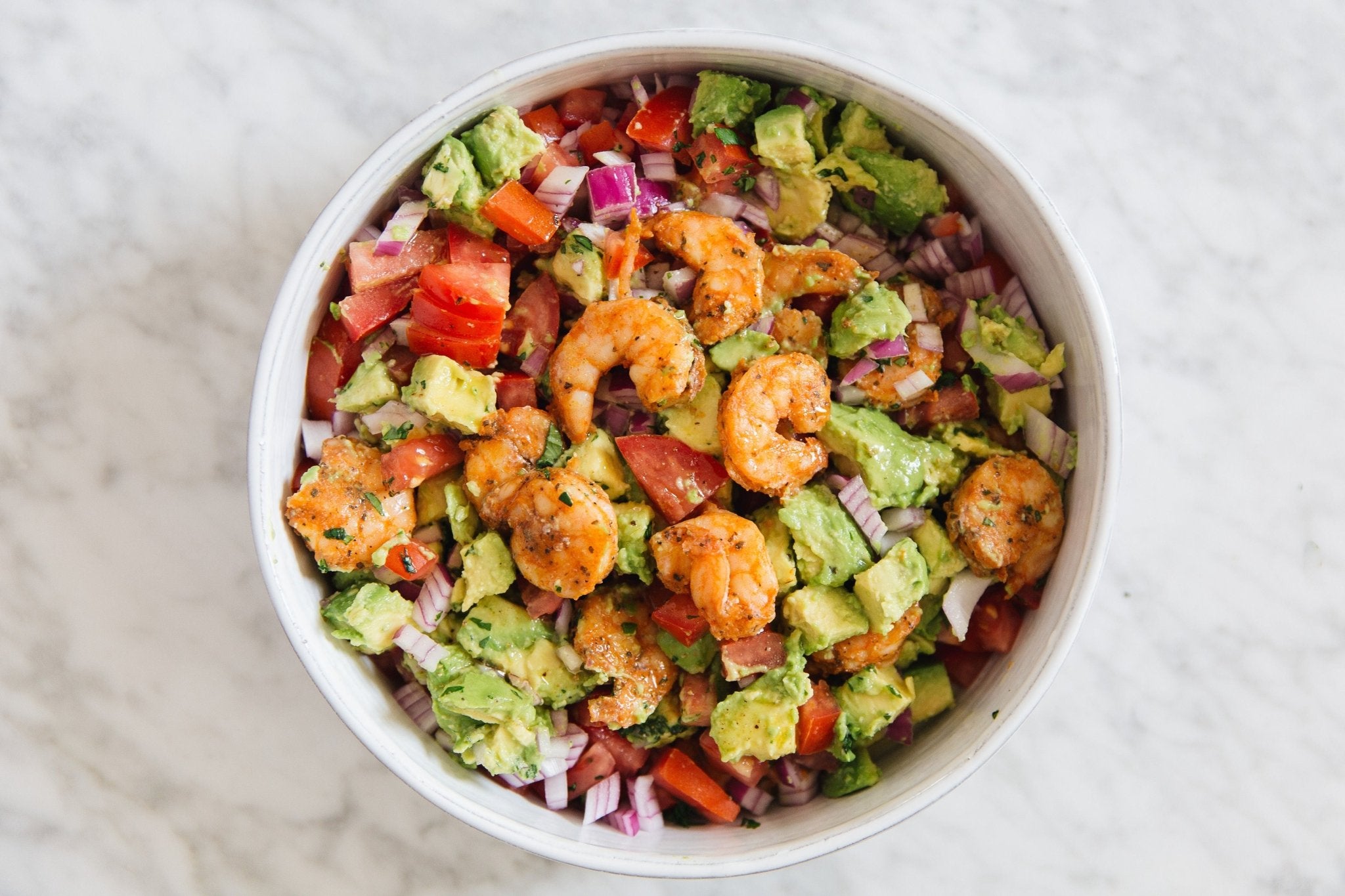 Prime Shrimp Signature Seasoned in white bowl with avocado, red peppers, and red onion. On marble counter. 